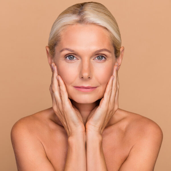 Photo of adorable confident woman naked shoulders hands arms cheeks empty space isolated beige color background confident woman after plastic surgery