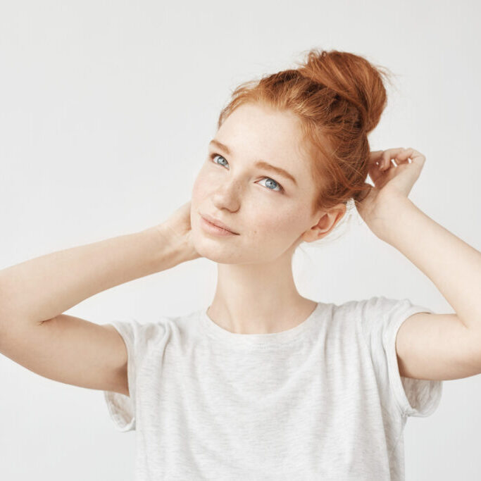 Portrait of tender redhead girl with hair bun and freckles smiling. otoplasty image